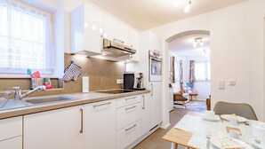 Una cocina moderna con armarios blancos, un lavamanos de acero inoxidable y un comedor con una mesa dispuesta para dos.