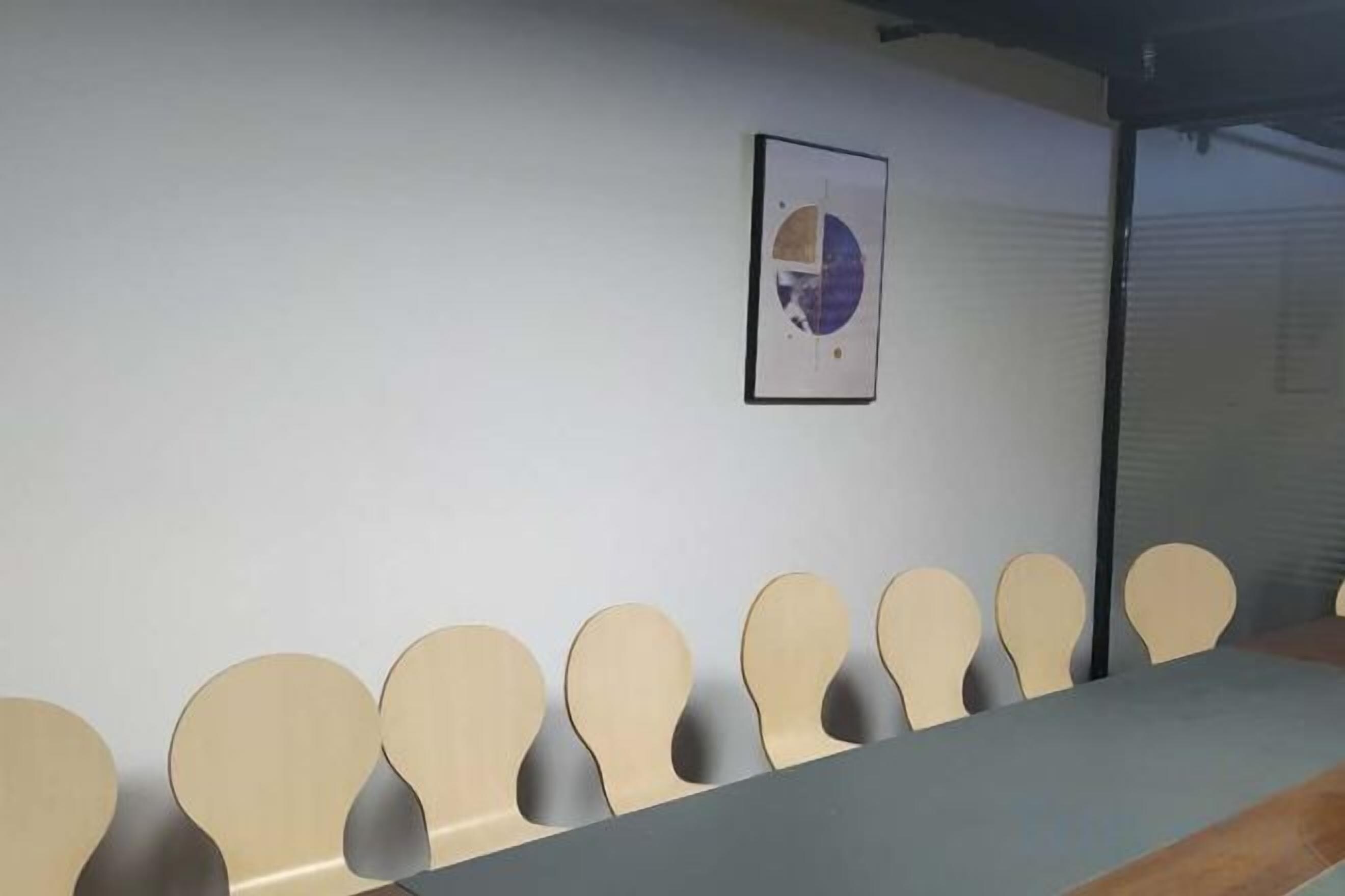 A row of beige chairs against a white wall with a framed picture above.