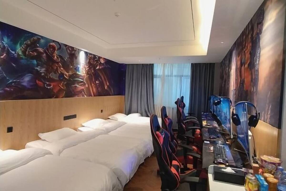 A hotel room with a large bed, gaming chairs, a desk with a computer, and a mural on the wall.