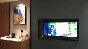 A television mounted on a dark wall, a wooden panel to the left, and a small counter with various items.