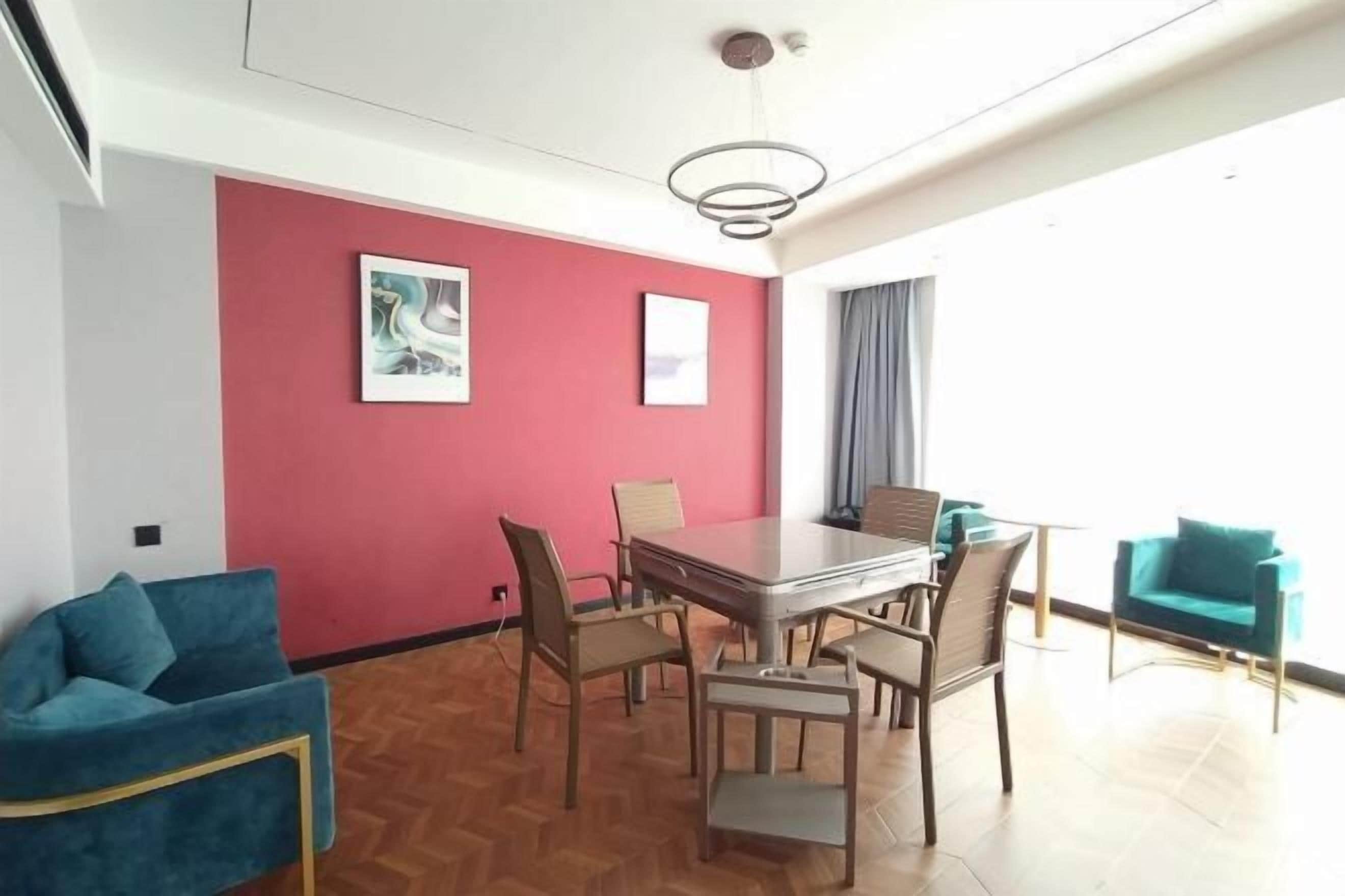 Una habitación moderna con una pared de acento roja, una mesa de comedor con sillas, un sofá y vistas al exterior.
