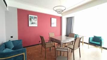 A modern room with a red accent wall, a dining table with chairs, a sofa, and a view of the outdoors.