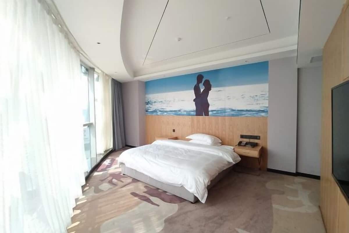 A hotel room with a bed, a nightstand, a painting of a couple on the wall, and a large window with curtains.