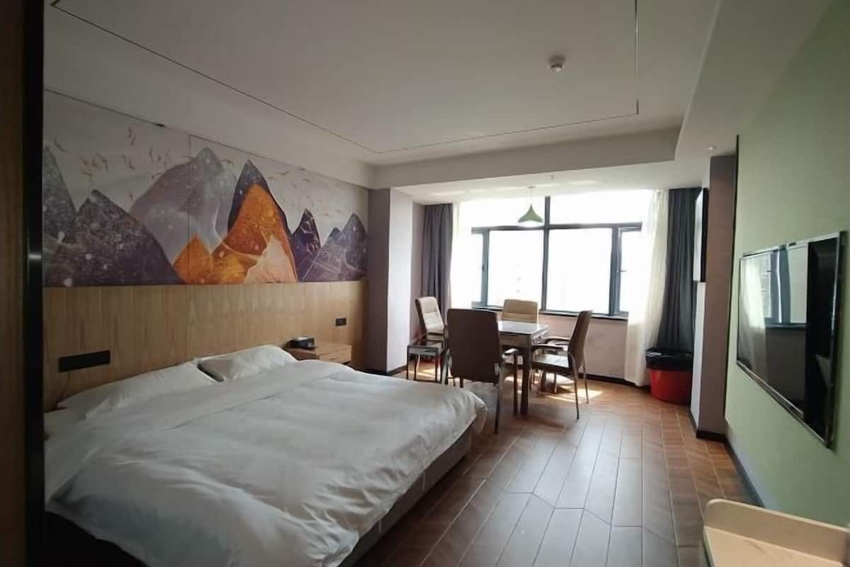 A hotel room with a large bed, a dining area with chairs, a table, and a TV.