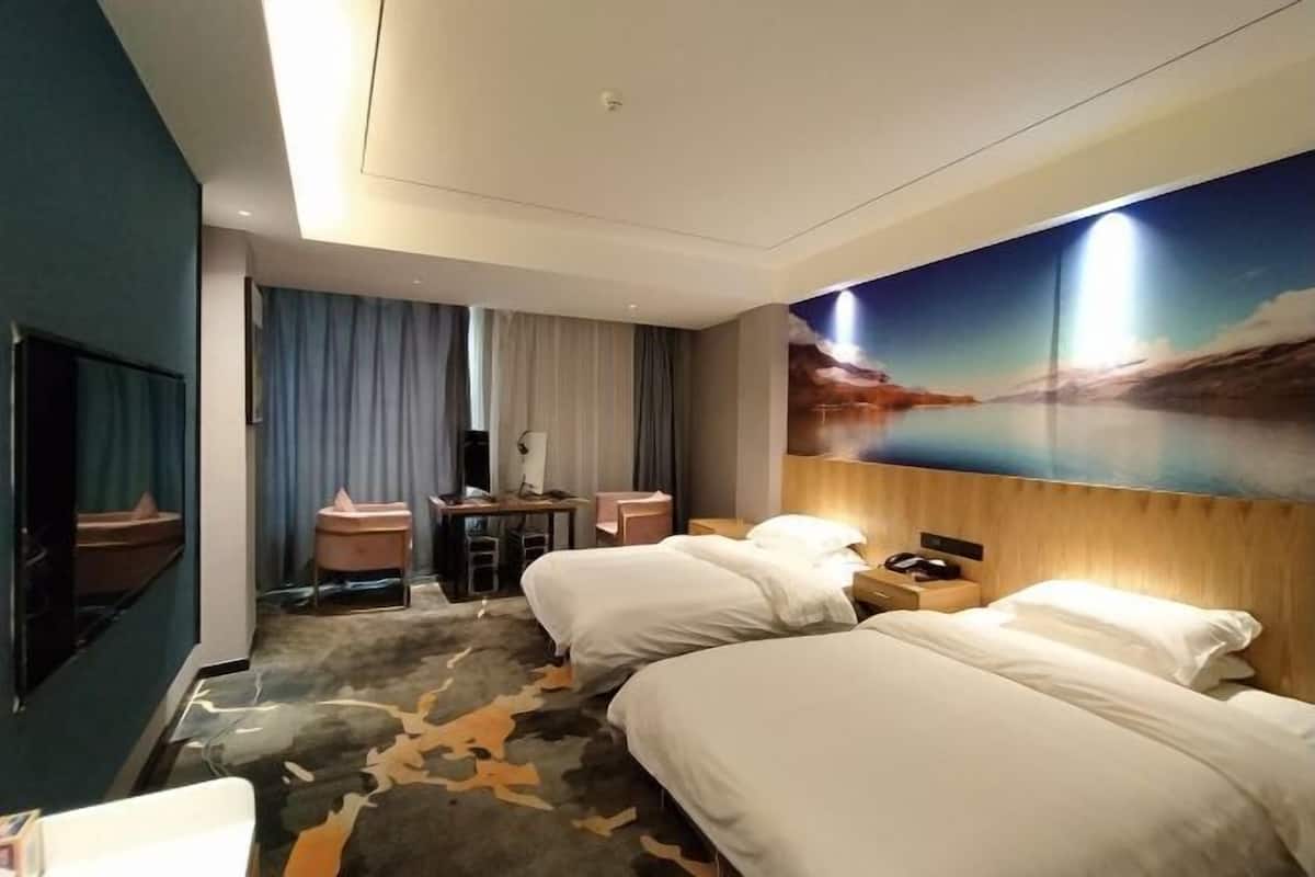 A hotel room with two beds, a desk, a TV, and a large painting of a sunset over water.