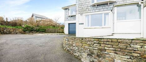 A two-story house with a stone wall and a paved driveway.