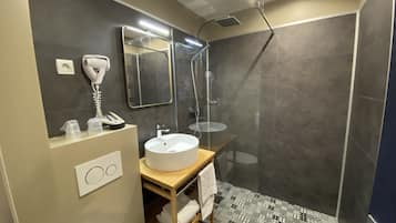 A modern bathroom with a large mirror, a white sink, a hairdryer, and a shower area.