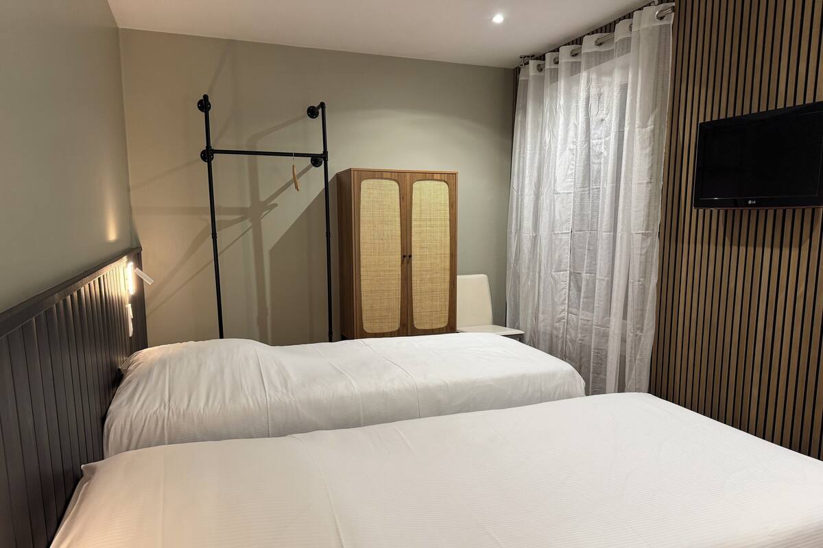 A hotel room with two beds, a wardrobe, a television, and a window with curtains.