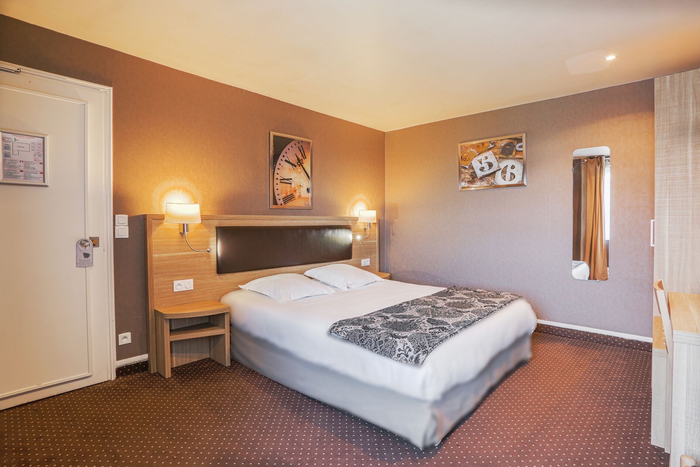 Une chambre d’hôtel avec un grand lit, deux tables de chevet, une horloge murale et un miroir.