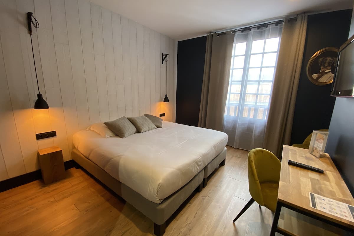 A bedroom with a bed, bedside lamps, a desk with a chair, and a window with curtains.