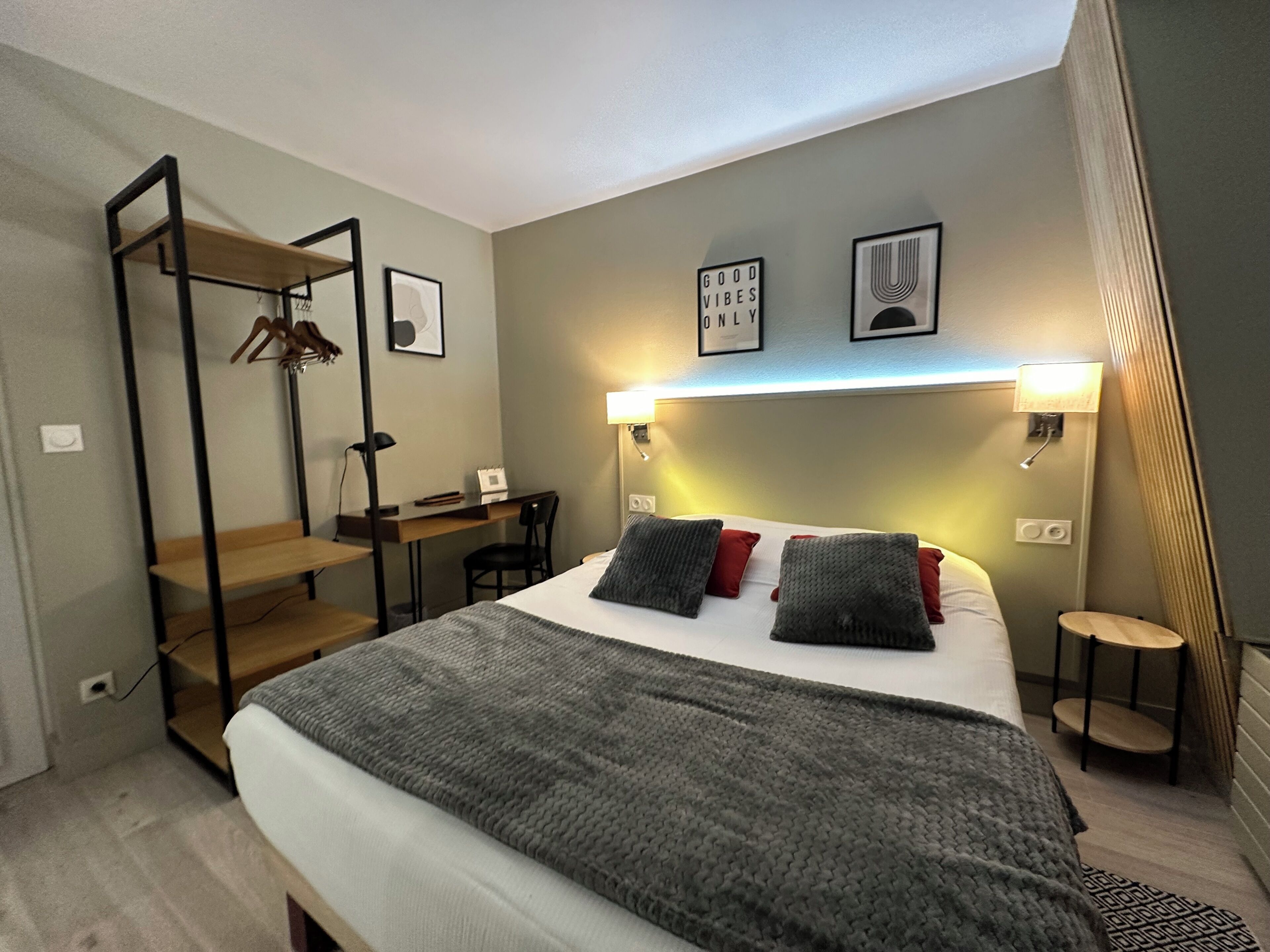 A bedroom with a bed, a desk, and a chair. There is a wall-mounted shelf with a spider decoration.