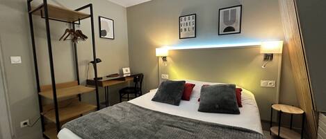 A bedroom with a bed, a desk, and a chair. There is a wall-mounted shelf with a spider decoration.