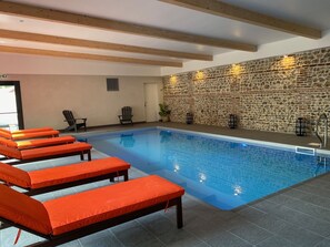A swimming pool with lounge chairs, a stone wall, and wooden beams. - Hotel SPA Piscine le Petit Castel (Beuzeville)