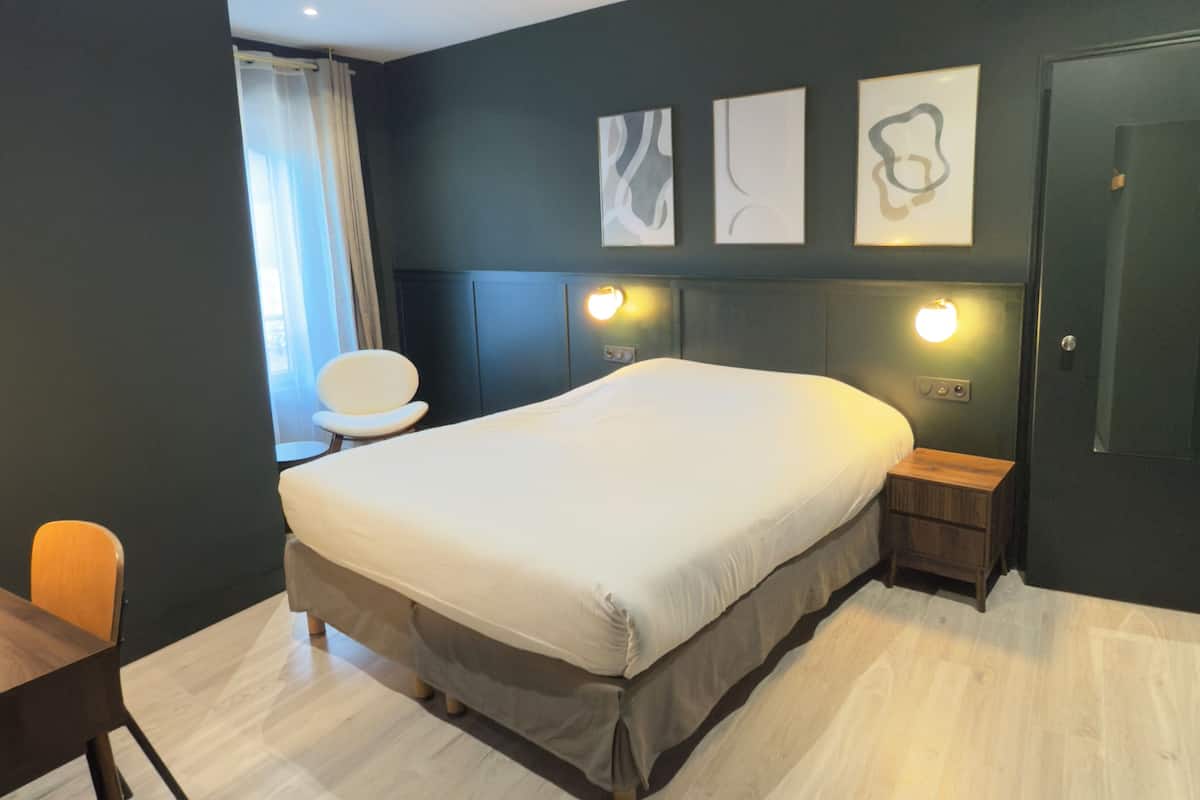 A modern bedroom with a large bed, bedside tables, a chair, and artwork on the wall.