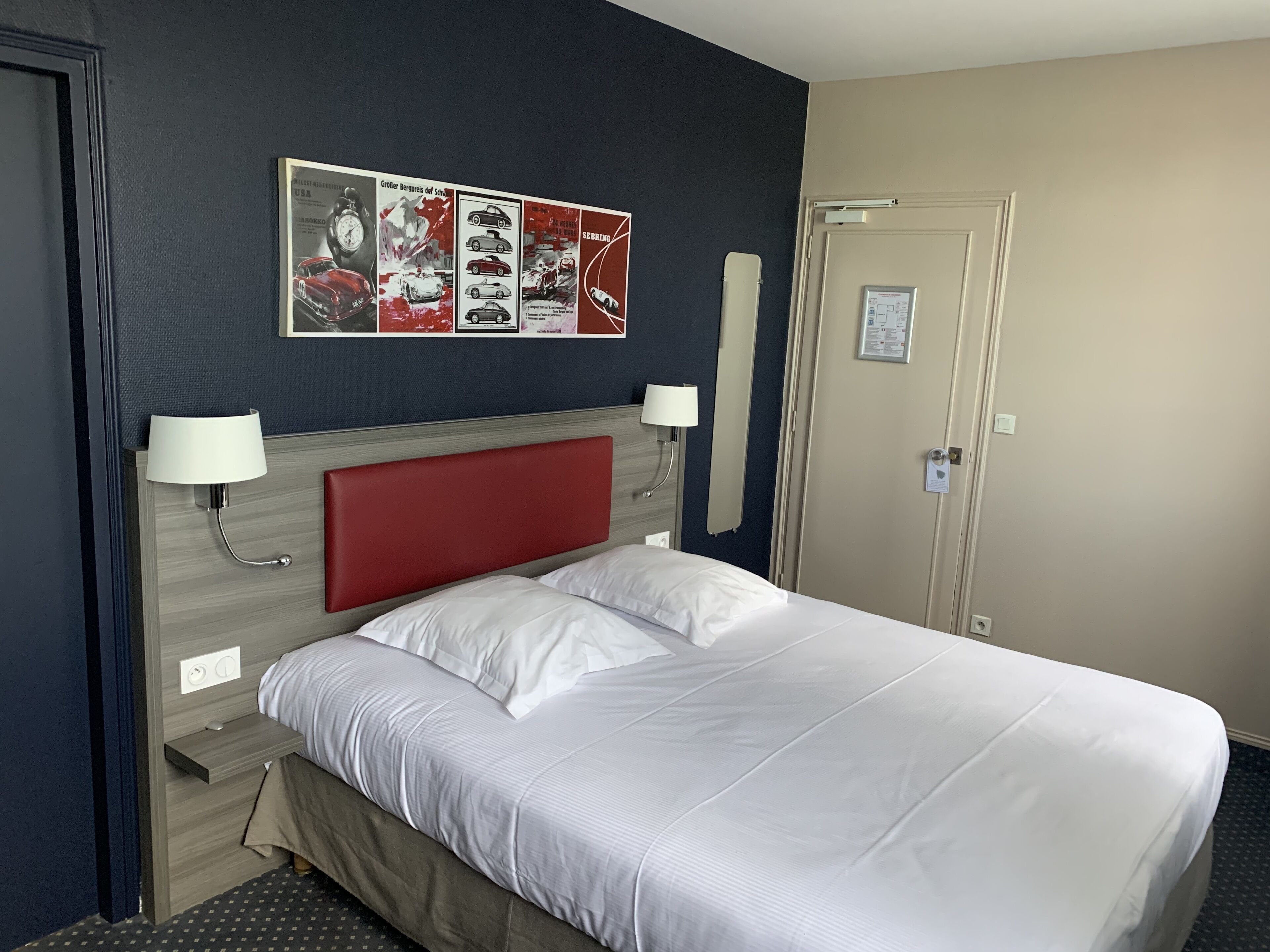 Habitación de hotel con cama, dos lámparas de noche, cabecera, un reloj de pared y una puerta.