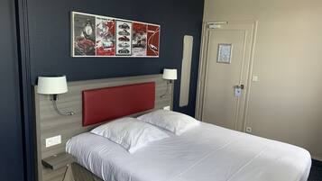 Habitación de hotel con cama, dos lámparas de noche, cabecera, un reloj de pared y una puerta.