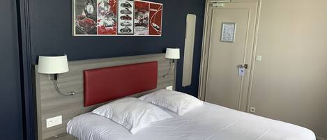 A hotel room with a bed, two bedside lamps, a headboard, a wall clock, and a door.