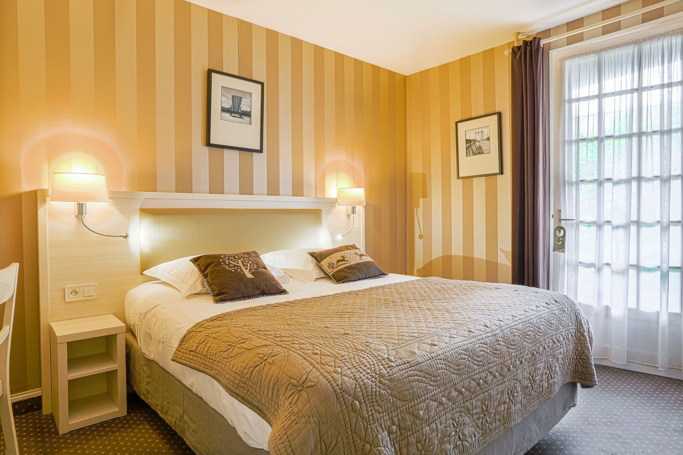 A hotel room with a large bed, two bedside lamps, a nightstand, and a window with curtains.