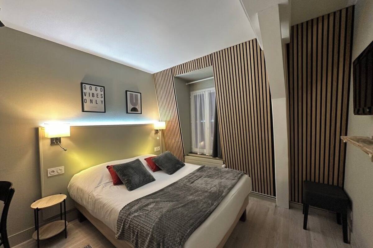 A modern bedroom with a bed, bedside tables, a small chair, and a wall-mounted shelf.