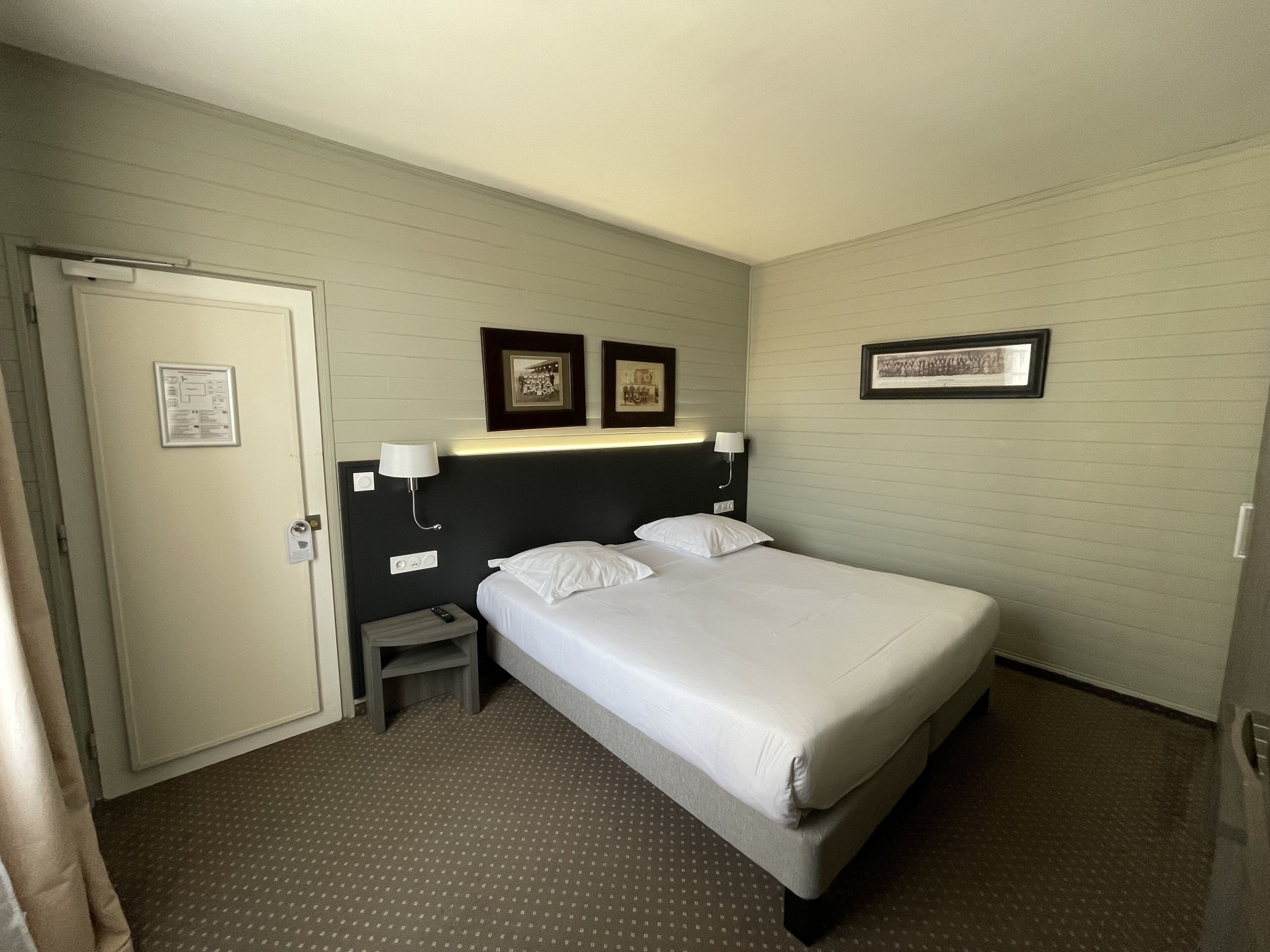 Ein Hotelzimmer mit einem Einzelbett, einem Nachttisch, einer Lampe und einem gerahmten Bild an der Wand.