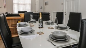 Comedor con una mesa blanca dispuesta para seis comensales, sillas negras y una botella de champán.