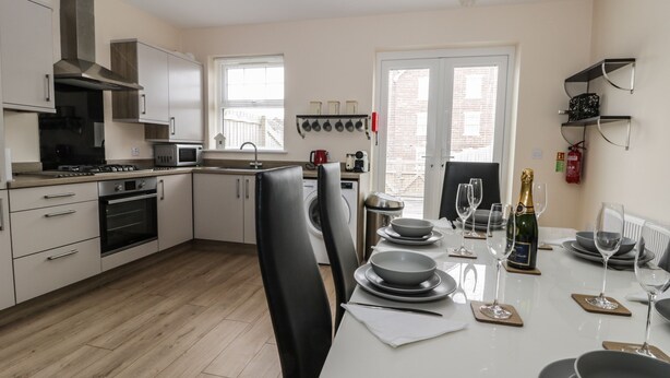 Una cocina moderna con armarios blancos, una campana extractora de acero inoxidable y un comedor con una mesa dispuesta para dos.
