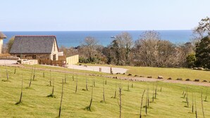 A stone building with a sloped roof overlooking a grassy field and the sea. - Apple Blossom Barn (Penzance)