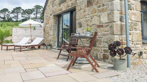 A stone building with a patio area featuring lounge chairs, a table, and a potted plant. - Apple Blossom Barn (Penzance)