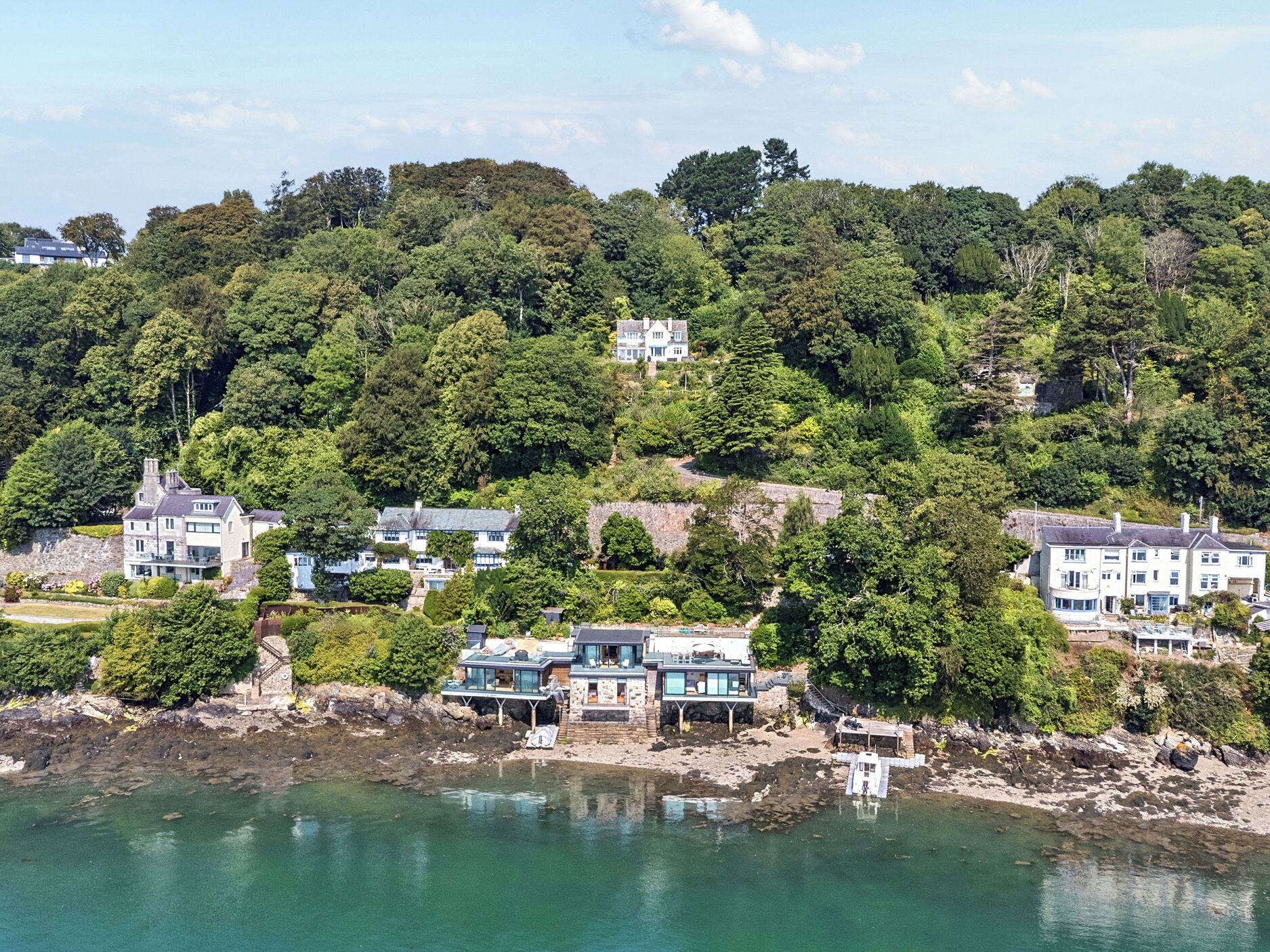 A coastal property with multiple buildings, including a large house with a prominent chimney, situated on a hillside overlooking a body of water.