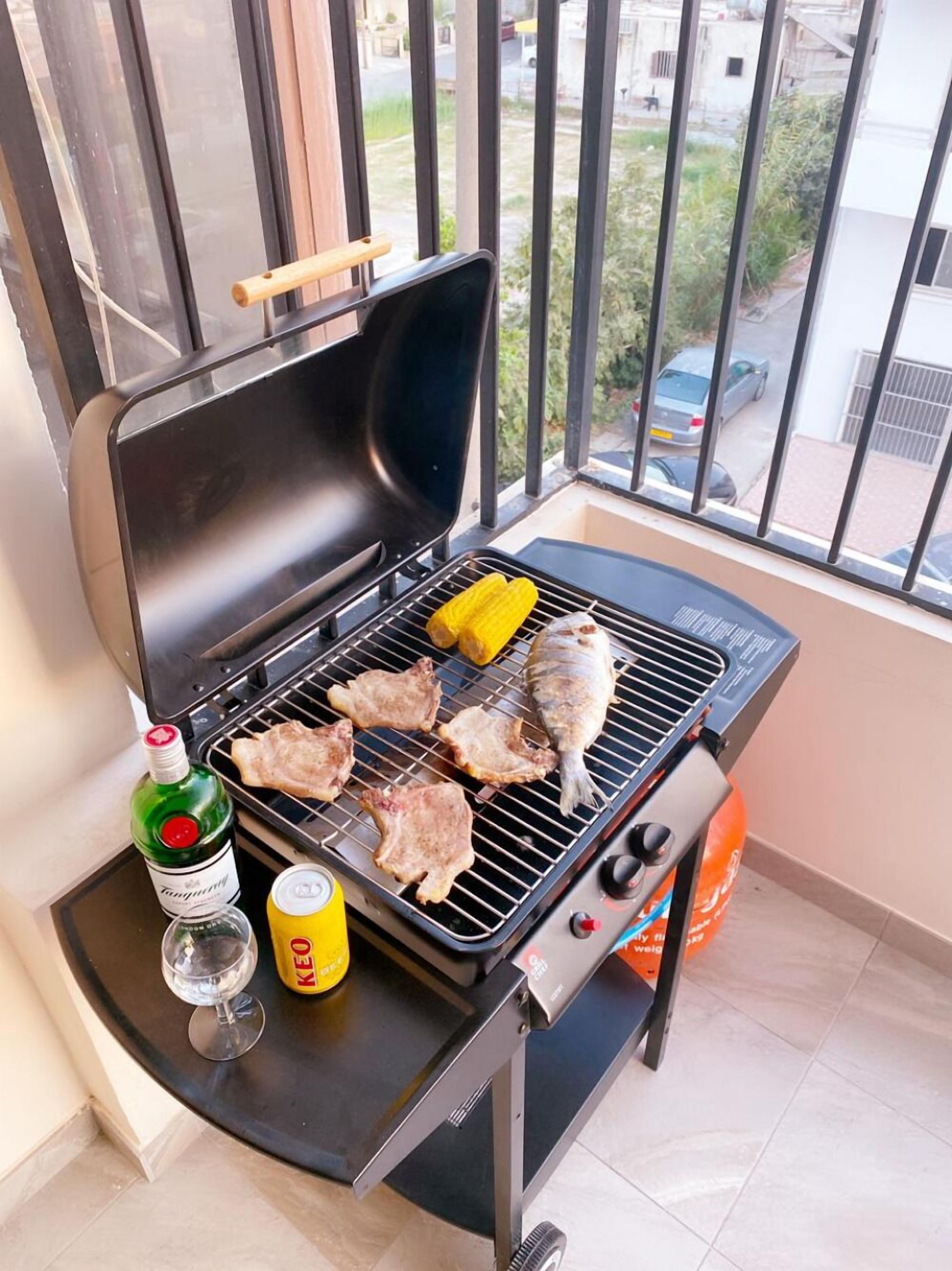 A balcony with a grill, a bottle of liquor, a glass, and a can.