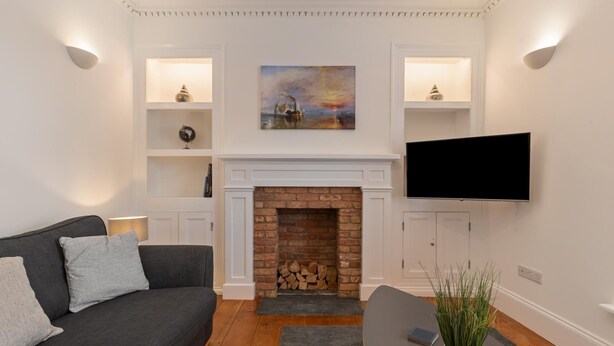 A living room with a fireplace, a sofa, a TV, and decorative shelves. - Falcon House in Pembroke Dock (Pembroke Dock)