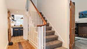 A staircase with a wooden handrail and carpeted steps leading to a room with a fireplace. - Falcon House in Pembroke Dock (Pembroke Dock)