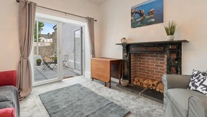 A living room with a fireplace, a sofa, a coffee table, and a sliding glass door leading to an outdoor patio. - Falcon House in Pembroke Dock (Pembroke Dock)