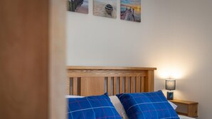 A bedroom with a wooden headboard, two blue plaid pillows, a white bedspread, and a nightstand with a lamp. - Falcon House in Pembroke Dock (Pembroke Dock)