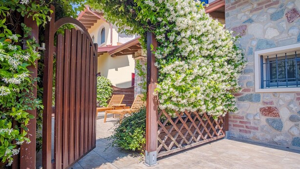 A stone building with a wooden gate and a pergola covered in white flowers. - Endless Summer Sirmione - Italian Homing (Sirmione)