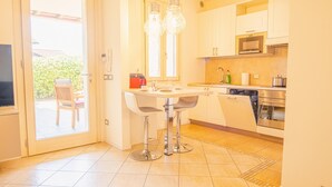 A modern kitchen with stainless steel appliances, a dining area with two chairs, and a sliding glass door leading to an outdoor seating area. - Endless Summer Sirmione - Italian Homing (Sirmione)