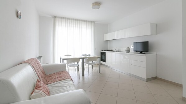 A modern, minimalist living room with a white sofa and a dining area with a table and chairs. - Residenza Excelsior 801 (Rocca San Giovanni)