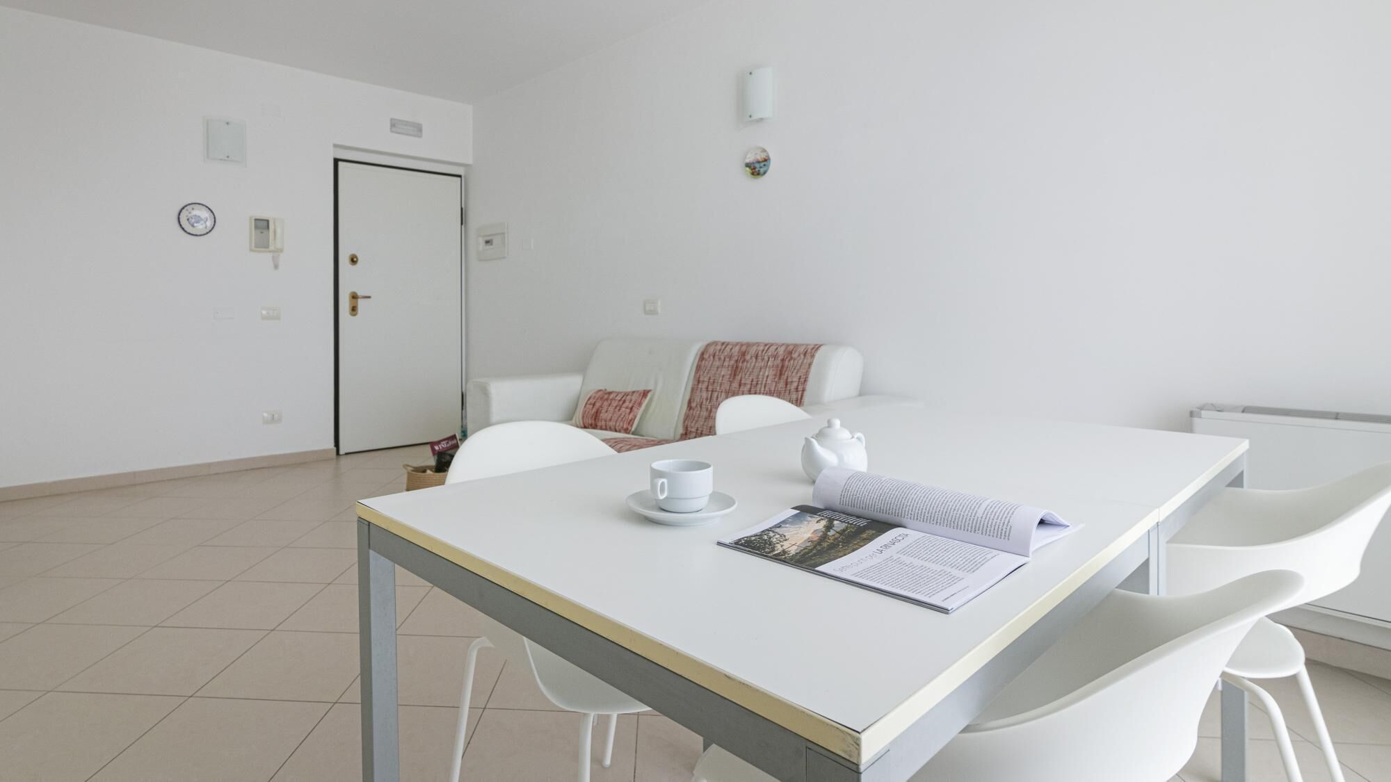 Una habitación minimalista con una mesa blanca, sillas, un sofá blanco y una puerta.
