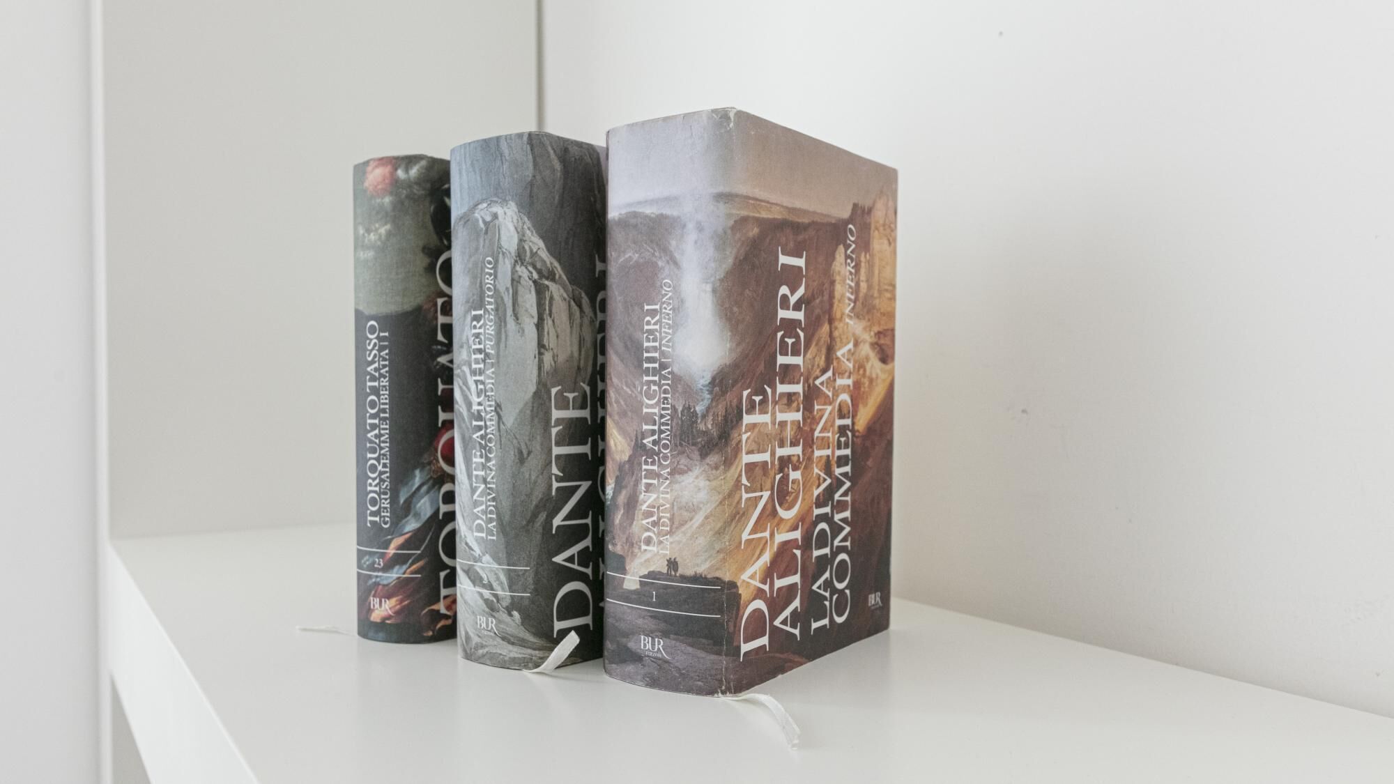 Un conjunt de tres llibres titulats 'DANTE ALIGHIERI' sobre una estanteria blanca.