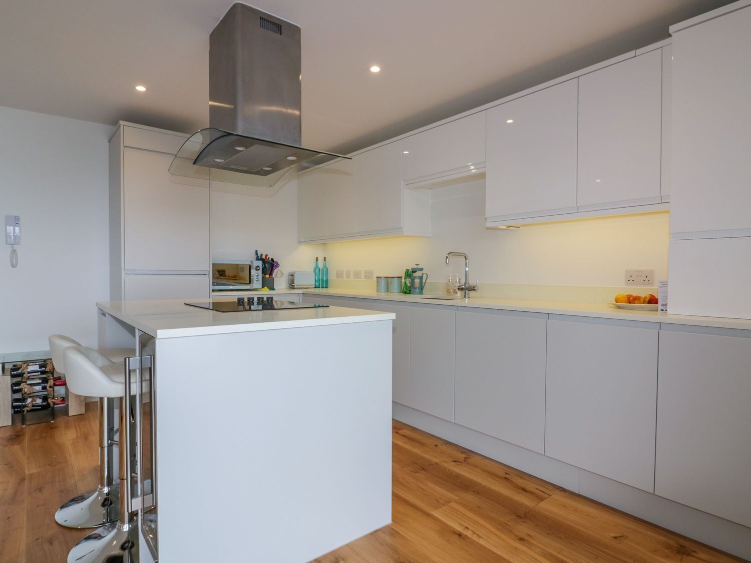 A modern kitchen with white cabinets, a stainless steel range hood, and a bar area with stools.