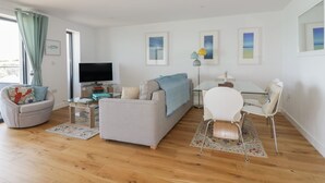 Un salon moderne comprenant un canapé, un fauteuil, un téléviseur et un coin repas avec une table et des chaises.