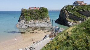 Une zone côtière avec une plage, une petite construction en bois portant l’inscription « Slush », et une maison située sur une falaise.