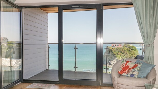 Un balcon avec vue sur la mer, une porte-fenêtre coulissante et un canapé agrémenté d’un coussin décoratif.