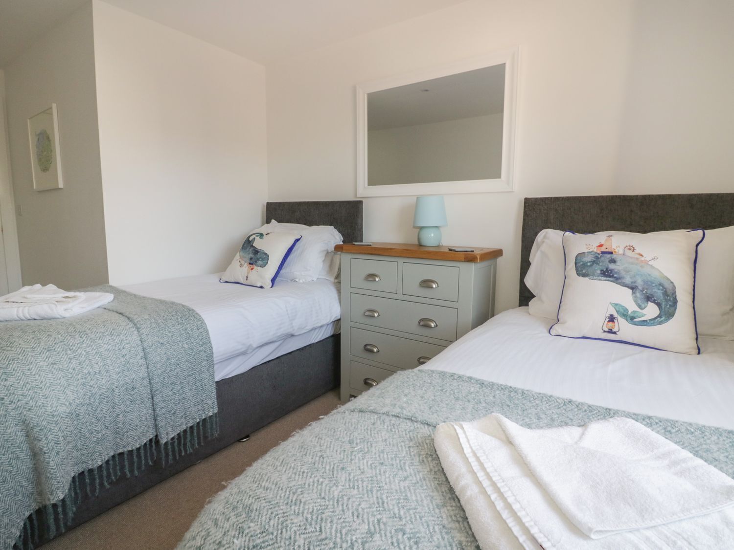 Une chambre à deux lits avec deux lits simples, une commode, un miroir et une lampe de chevet.