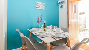 A dining area with a turquoise wall, a painting of boats, and a door leading outside.