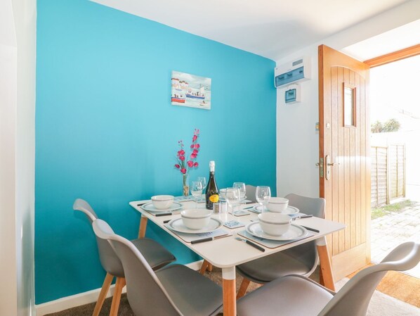 Un coin repas avec un mur turquoise, une table dressée pour quatre personnes et une porte donnant sur un espace extérieur.