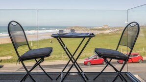 A balcony with two chairs and a table, overlooking a beach and a road with a red car. - Fistral Watch (Newquay)