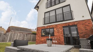A two-story house with a brick facade, a balcony, and a patio with outdoor furniture. - The Hideaway Beach House (New Romney)