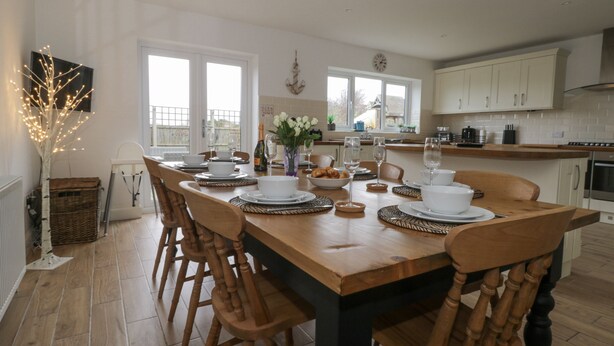 A dining area with a wooden table set for six, surrounded by wooden chairs. - The Hideaway Beach House (New Romney)