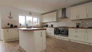 A spacious kitchen with white cabinetry, a central island, and a large window providing natural light. - The Hideaway Beach House (New Romney)